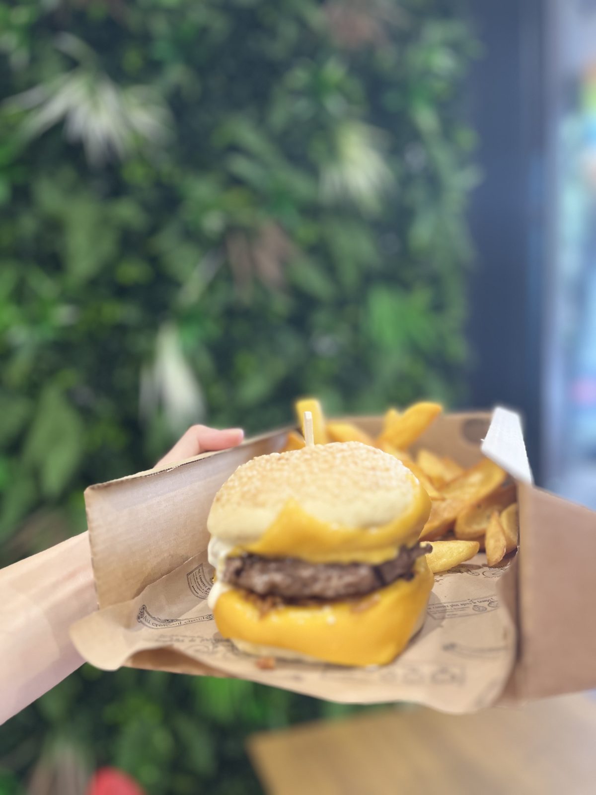 Cheese burger tenu à la main devant le mur végétal